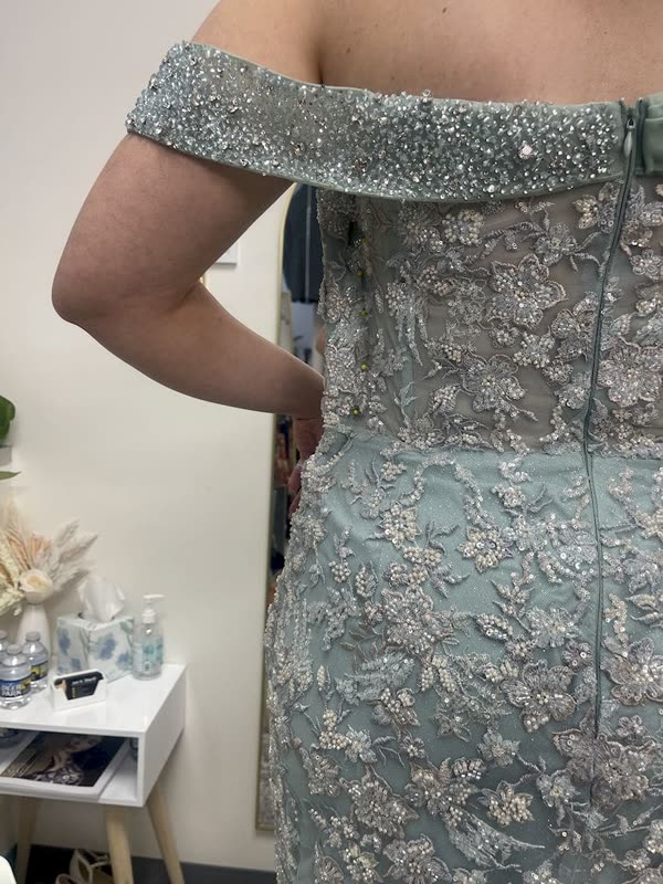Close view of the beaded off-shoulder band and back zip of a sage green gown during fitting.