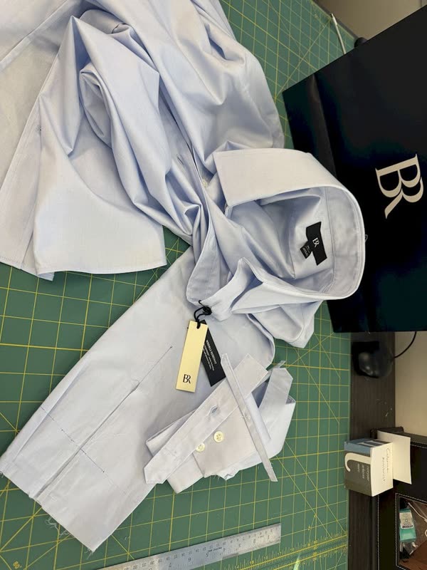 A pale blue shirt laid out on the green cutting mat with the sleeve chalked and a steel ruler alongside.